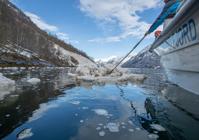 Lokal guide peker mot Naoberadn fjellside, sted for gammelt sagn, omgitt av snøflak etter et ras i hypernatur fjord