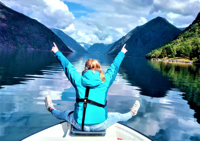 Embracing pure joy and digital detox in the majestic Sognefjord, a guest sits at the bow of the boat, arms open wide to the mountain peaks and the open water.