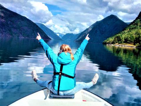Embracing pure joy and digital detox in the majestic Sognefjord, a guest sits at the bow of the boat, arms open wide to the mountain peaks and the open water.