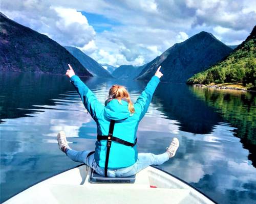 Embracing pure joy and digital detox in the majestic Sognefjord, a guest sits at the bow of the boat, arms open wide to the mountain peaks and the open water.