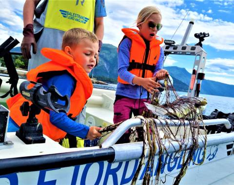 "Children learning traditional gillnet fishing in Balestrand, Norway, with Captain Tor. Kids discovering a fresh catch in the net on a boat in the Sognefjord."