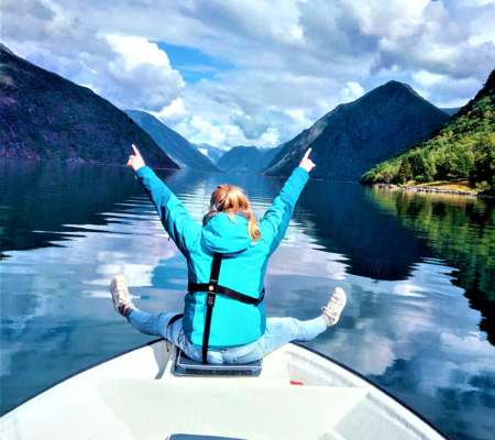 Cheerful prank in Fjærlandsfjord lady sitting on the bow and happy on a fishing trip and high mountains with clear water