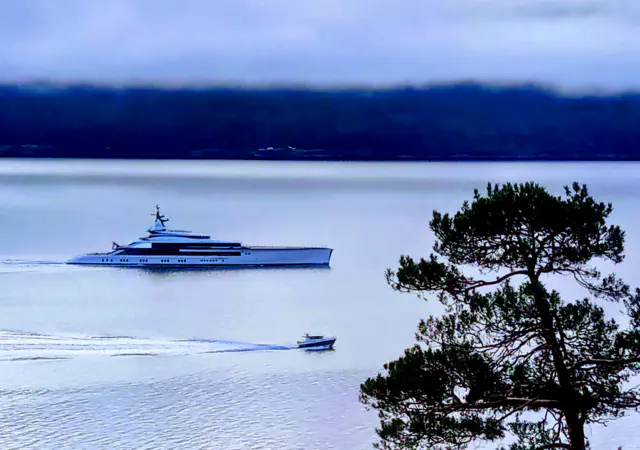 Superyacht 'Bravo Eugenia' next to a small boat in the Sognefjord, illustrating 3D luxury versus 5D authentic experience.