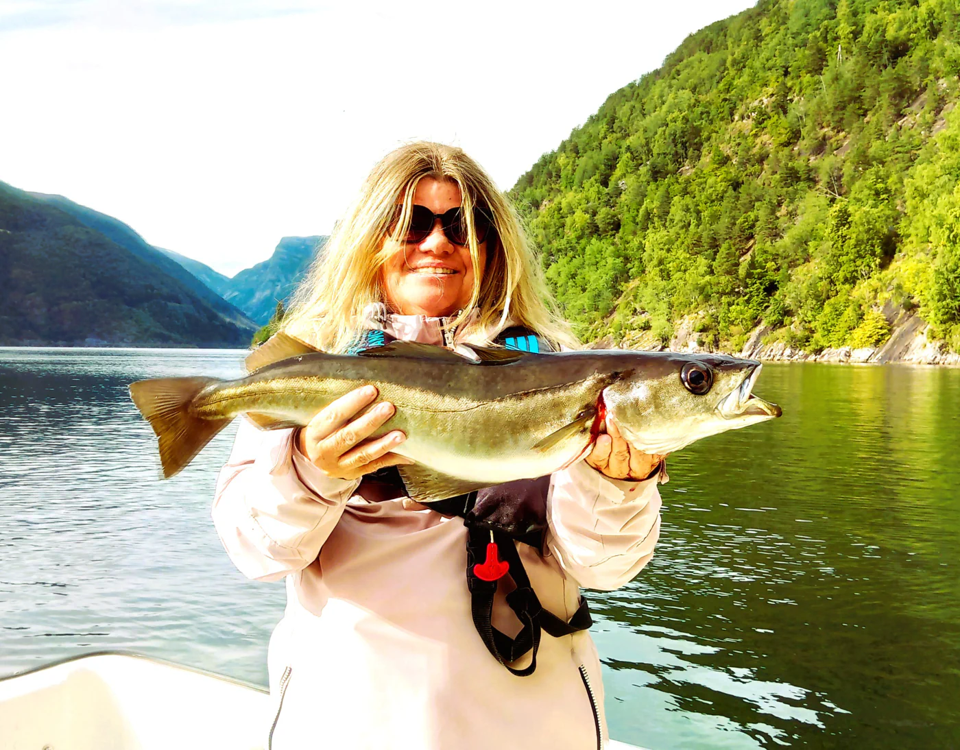 smiling woman with fishing rod and red jacket fishing in Esefjorden Norway with captain Tor among high mountains in Sognefjorden