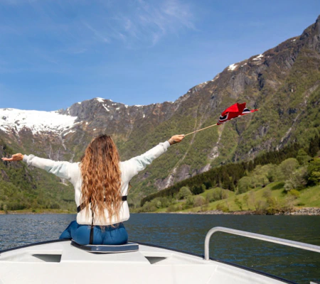 Woman enjoying a private boat tour on the Sognefjord, surrounded by steep mountains and flying a small Norwegian flag.