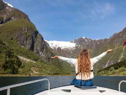 Woman enjoying a private boat tour on the Sognefjord, surrounded by steep mountains and flying a small Norwegian flag.